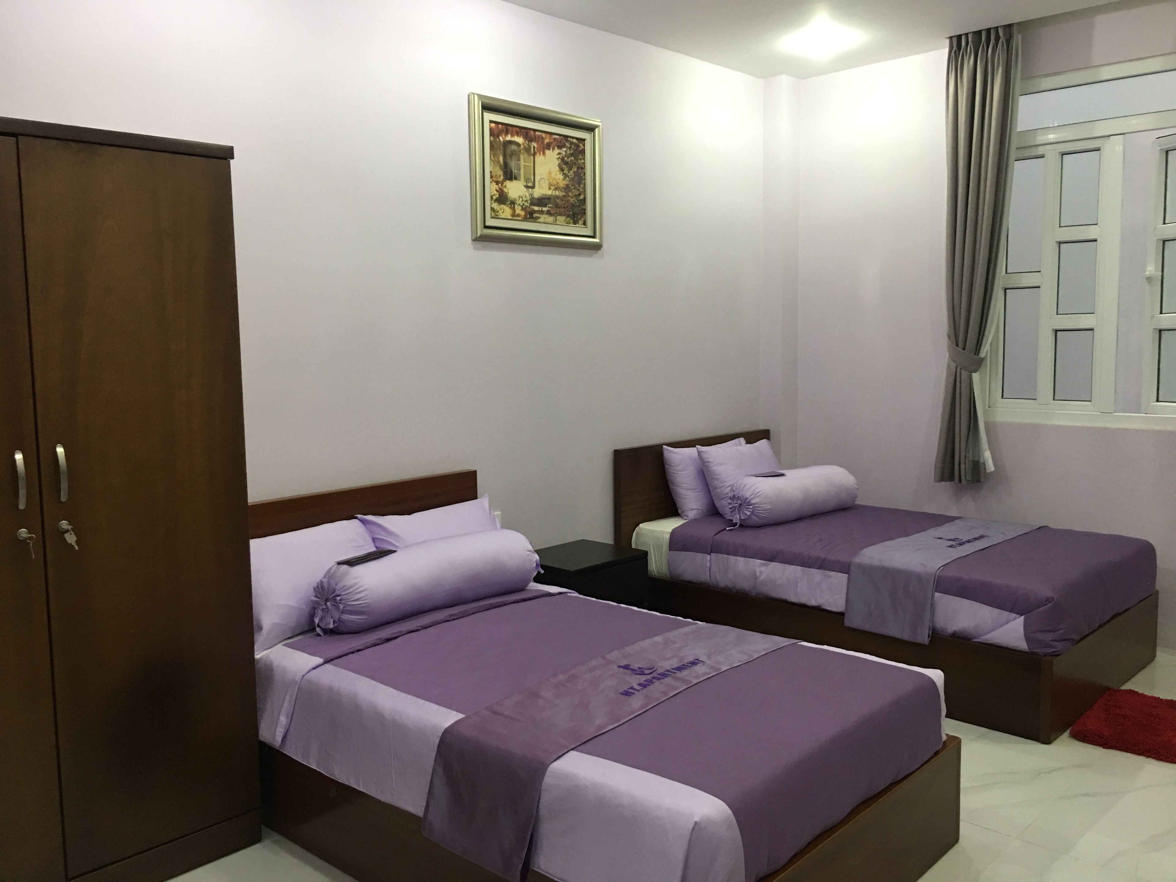 A hotel room with two beds, a wardrobe, a painting on the wall, and a window with curtains.