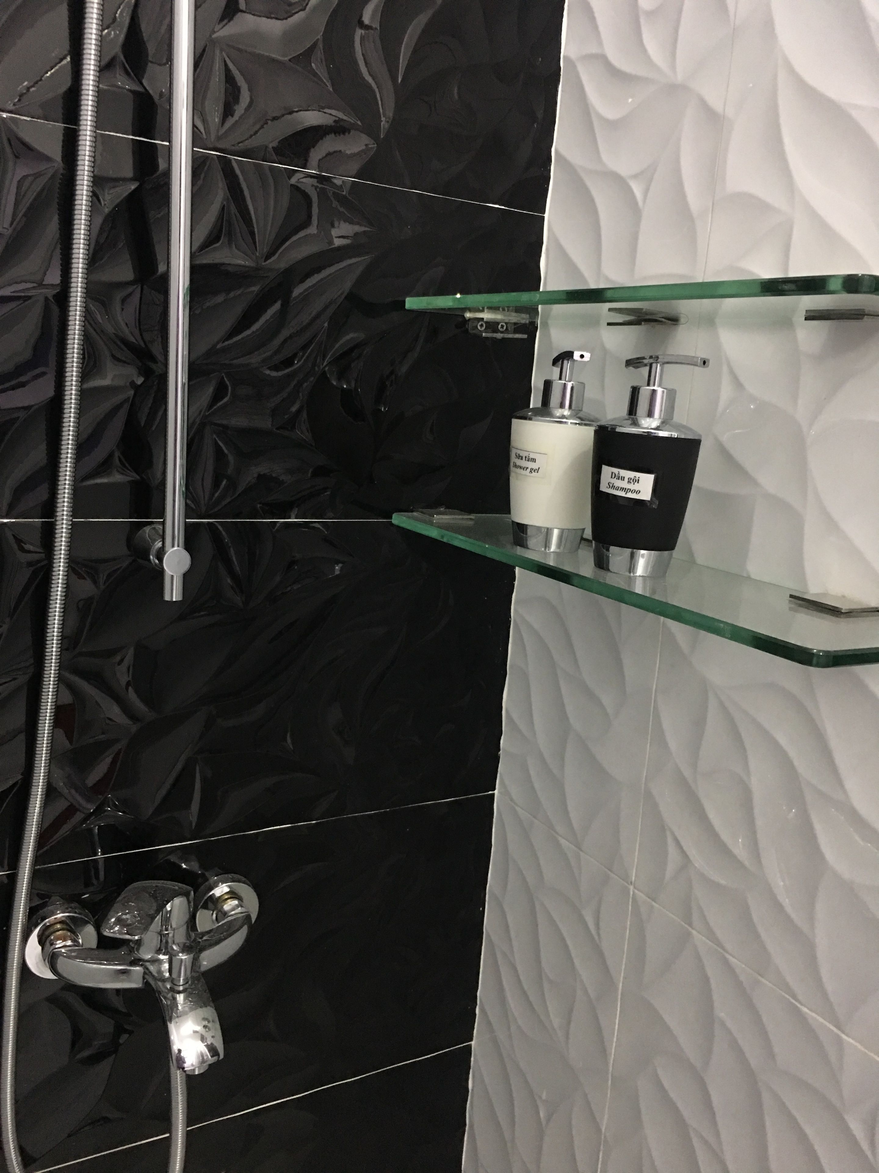 Et badeværelse med vægge i sort og hvidt mønster, en glashylde med toiletartikler og en bruser med en kromslange.