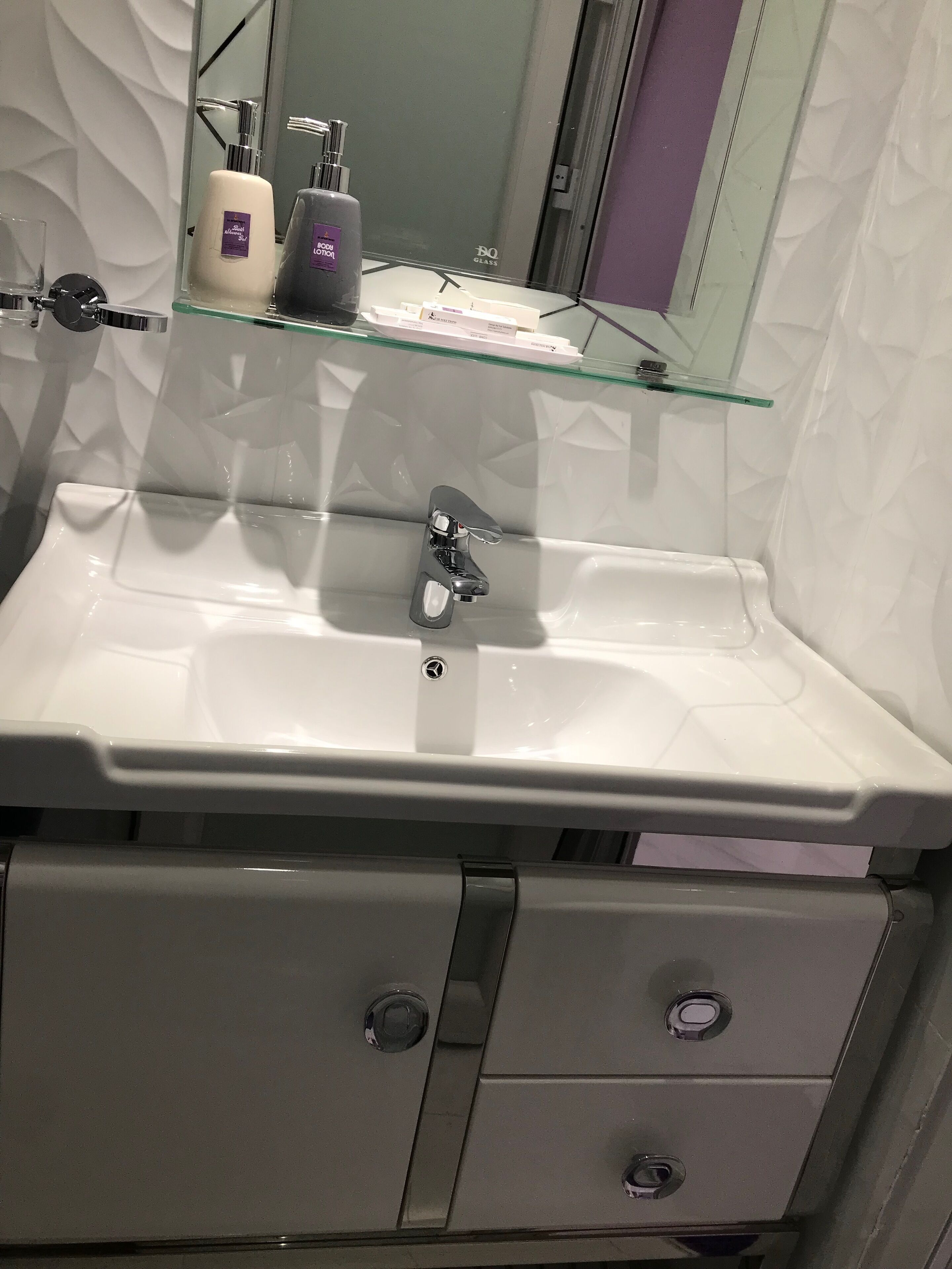 Ein Badezimmer mit einem weißen Waschbecken, einem Spiegel und einer Glasablage mit Pflegeprodukten.