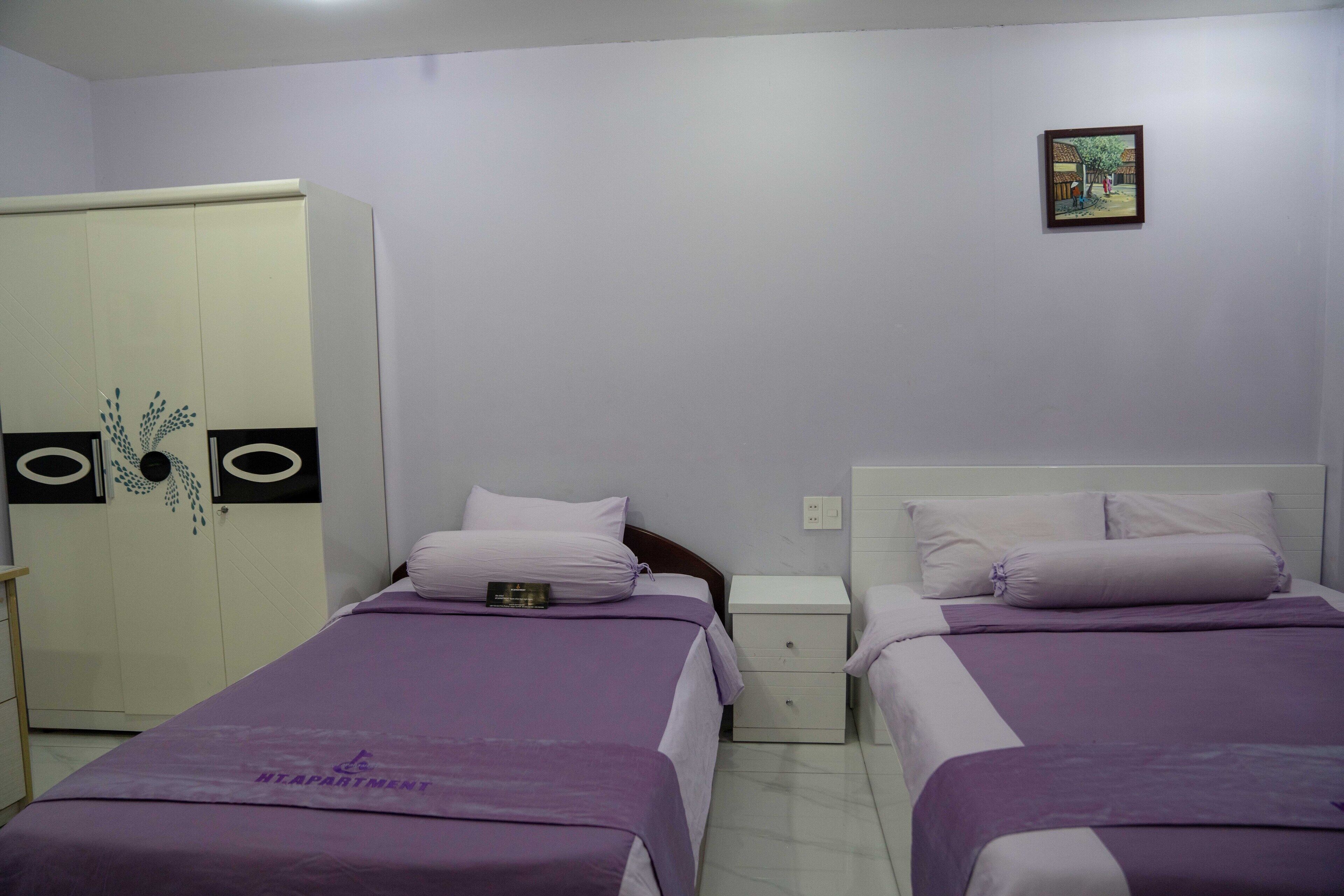 A bedroom with two beds, a wardrobe, a nightstand, and a wall-mounted picture.