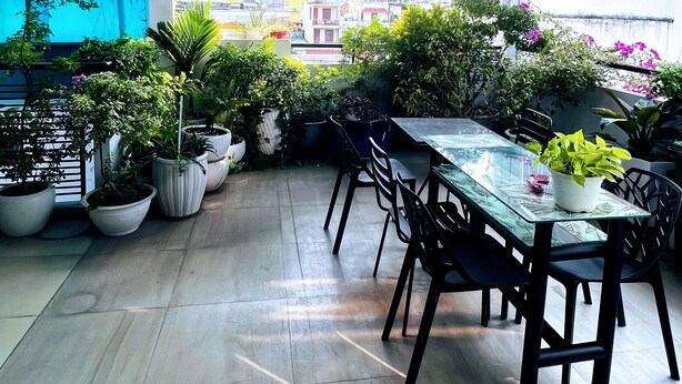 An indoor patio with a glass table and chairs, surrounded by potted plants and a view of the cityscape. - HT Hotel Apartment (Ho Chi Minh City)