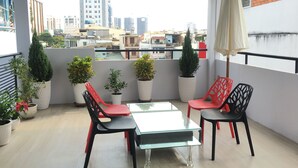 A balcony with potted plants, red and black chairs, and a glass table. - HT Hotel Apartment (Ho Chi Minh City)