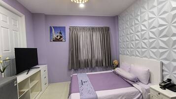 A bedroom with a bed, a television, a desk, and a patterned wall.
