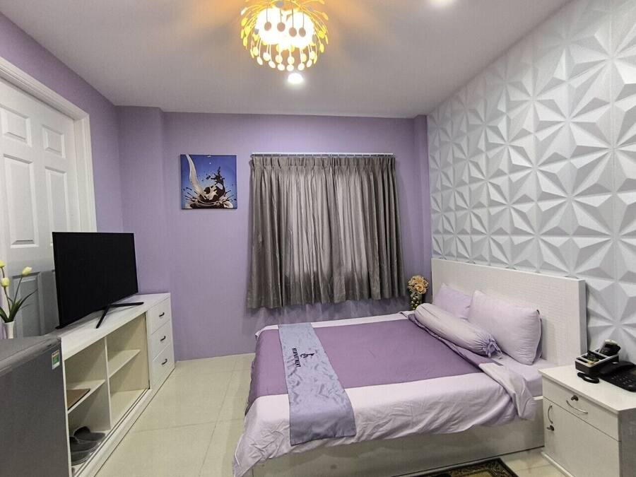 A bedroom with a bed, a television, a desk, and a patterned wall.