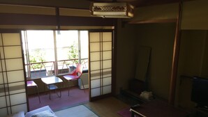 A traditional Japanese room with tatami flooring, a futon bed, a small table, a chair, and a sliding door leading to an outdoor area with a table and chairs. - Miyoshiya Ryokan (Tanabe)