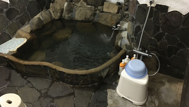 A stone hot tub with a faucet and showerhead, surrounded by stone walls. - Miyoshiya Ryokan (Tanabe)