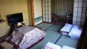 A traditional Japanese room with tatami flooring, a low table with a floral tablecloth, a bed with white bedding, and a sliding door leading to a balcony. - Miyoshiya Ryokan (Tanabe)