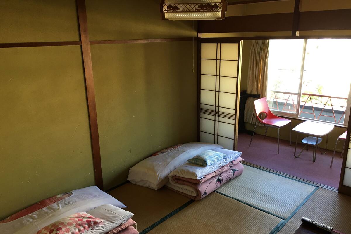 A traditional Japanese-style room with tatami flooring, a futon bed, a small table, and a chair.