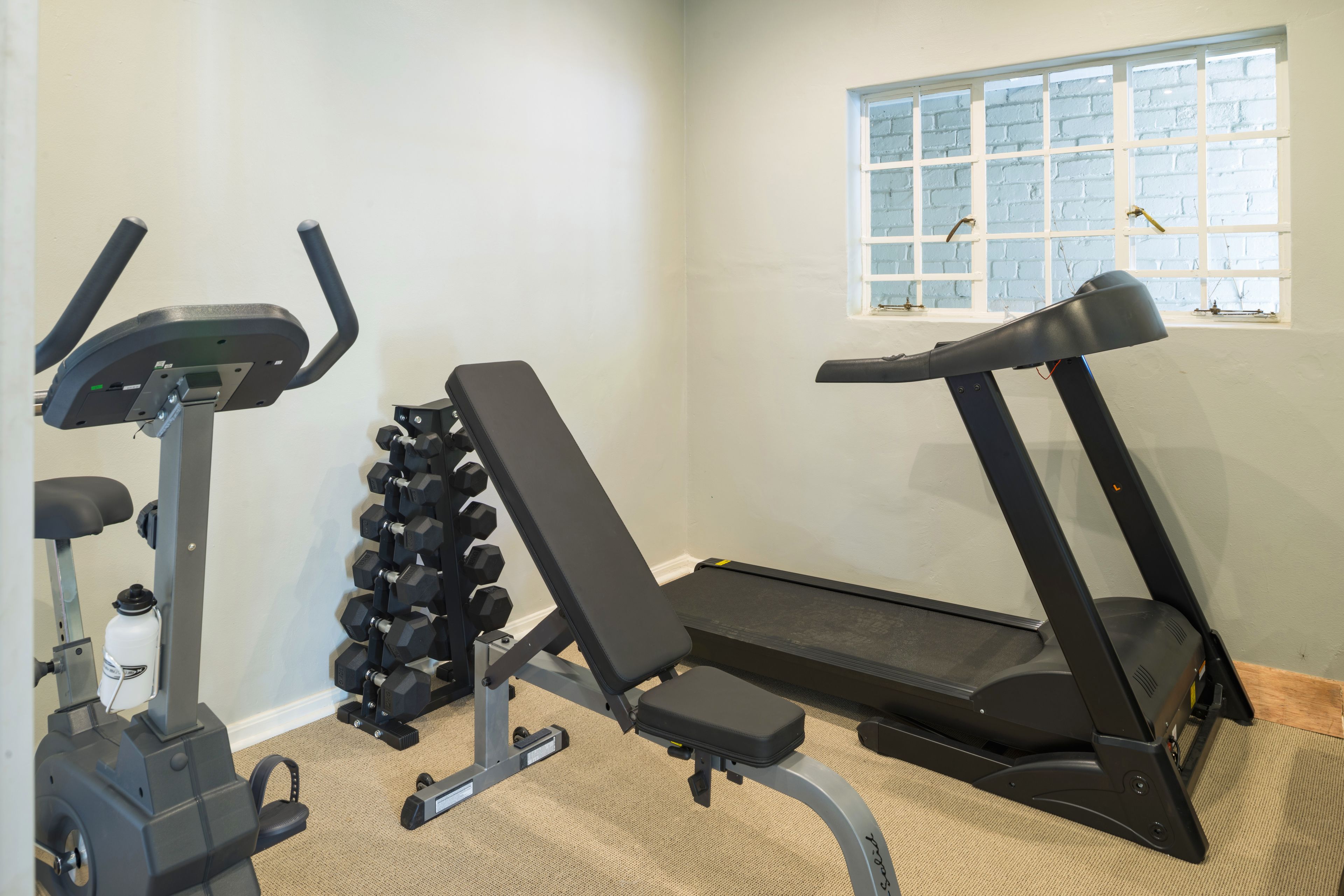 Un gimnasio en casa con bicicleta estática, banca de pesas, mancuernas y cinta de correr.