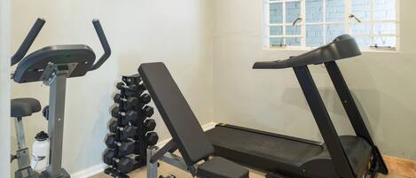 Un gimnasio en casa con bicicleta estática, banca de pesas, mancuernas y cinta de correr.