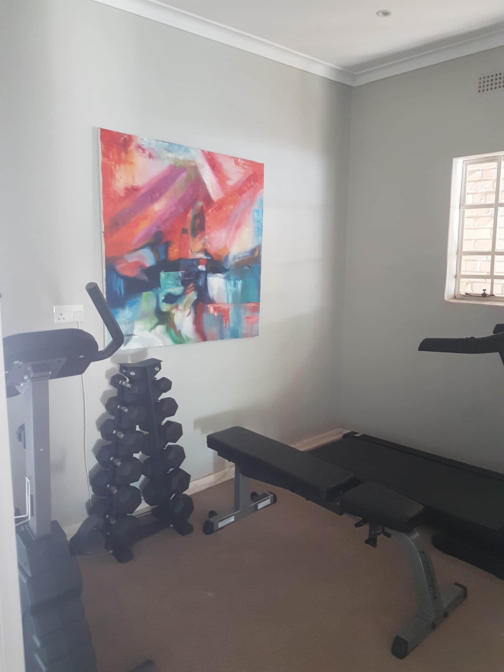 A gym with exercise equipment, a bench, and a colorful abstract painting on the wall.