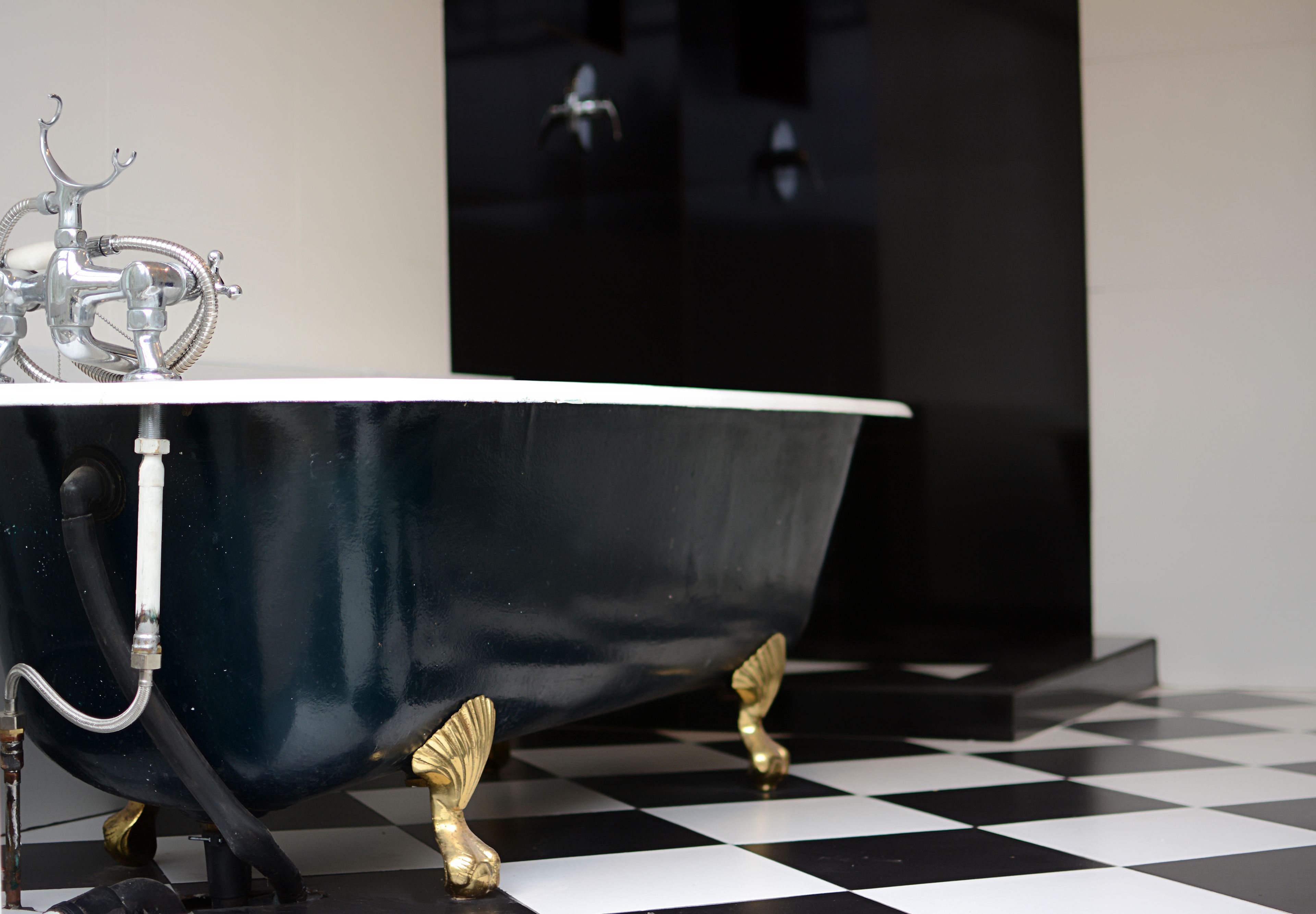 Una bañera con patas doradas y un grifo, sobre un piso a cuadros.
