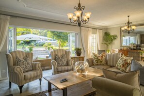 A spacious living room with a large window, a chandelier, and a dining area. - Number Eighteen Exclusive Guest Lodge (Harare)