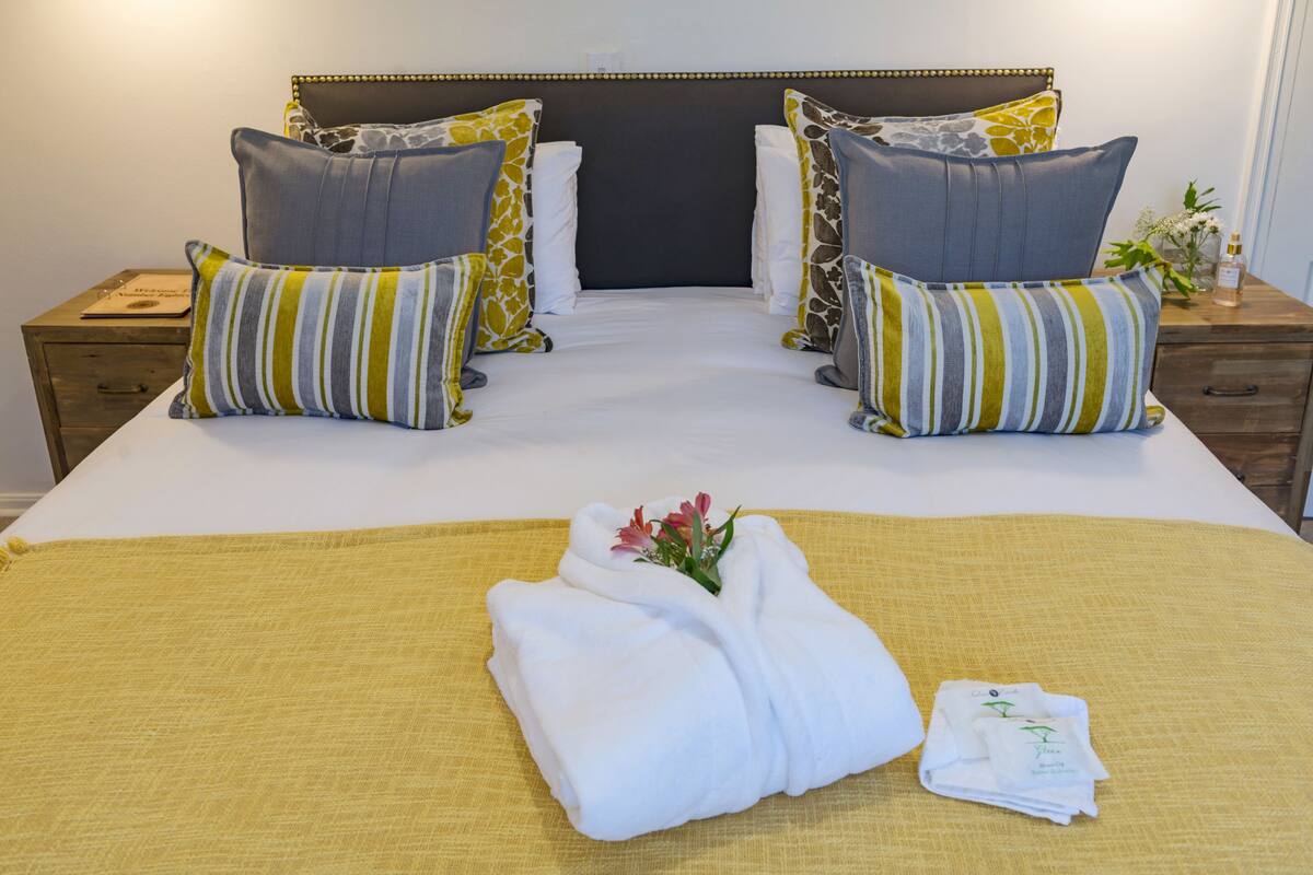 A neatly made bed with striped pillows, a folded towel, and a small bouquet of flowers.