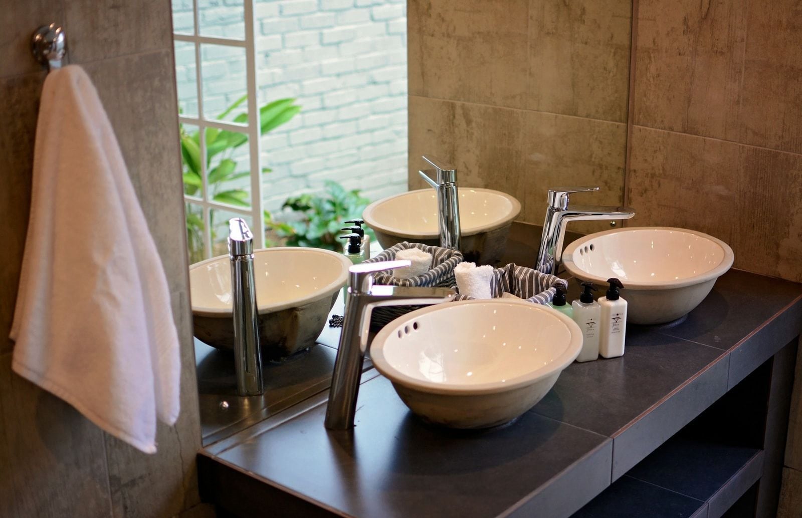 A bathroom with three large sinks, a mirror, and a towel rack.