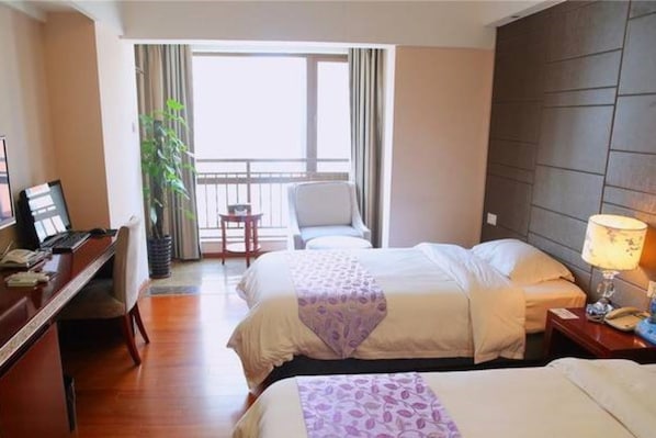 Habitación de hotel con dos camas, un escritorio con ordenador, una silla y un balcón con cortinas.