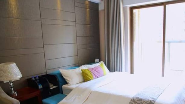 A hotel room with a bed, a blue sofa, a lamp, and a window with curtains. - YUMI Apartment-Pujun Station Branch (Foshan)