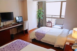 Habitación de hotel con cama, escritorio, computadora, televisor, silla y balcón con vistas.