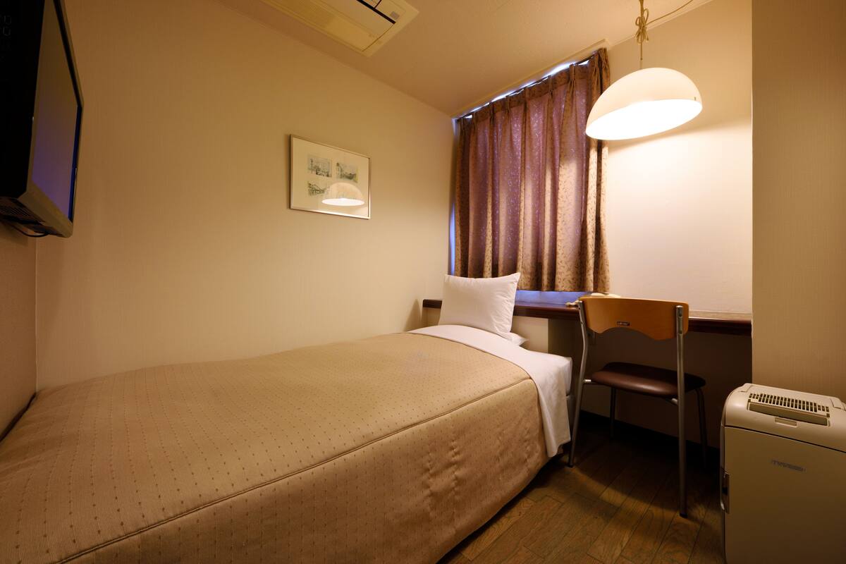 A small, neatly arranged bedroom with a single bed, a desk, and a chair.