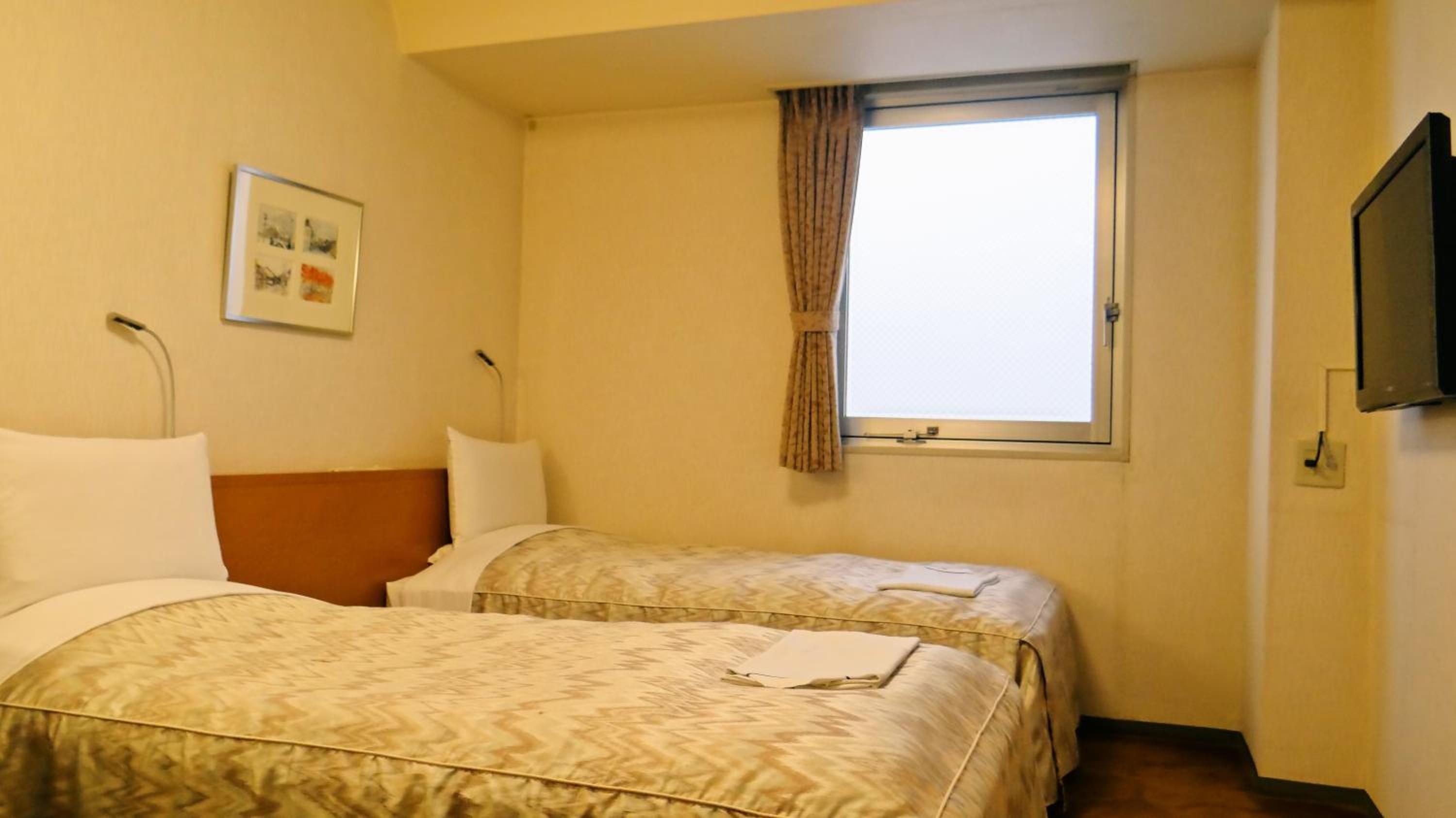Habitación de hotel con dos camas, una ventana con cortinas, un televisor de pantalla plana montado en la pared y un cuadro enmarcado.