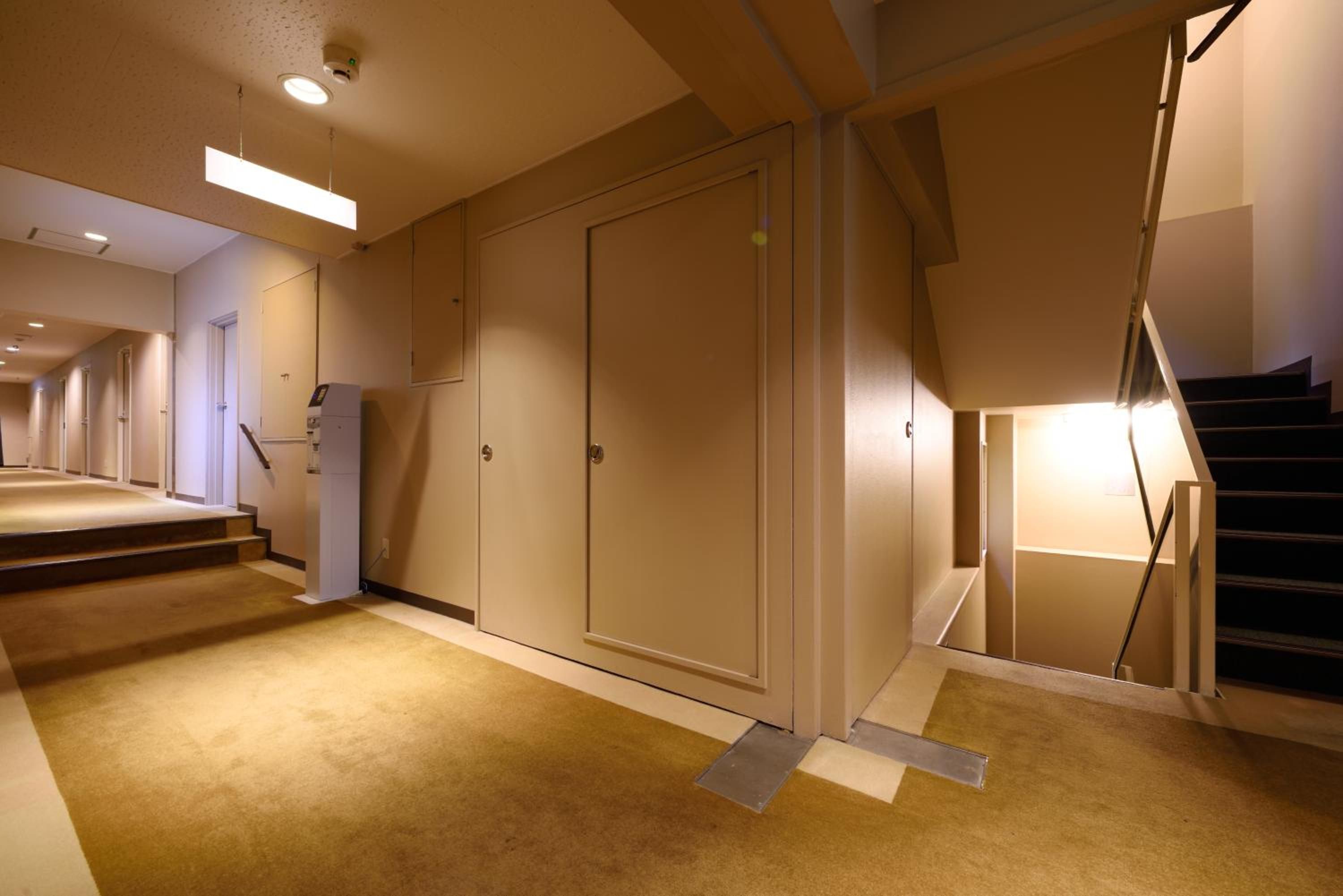 A hotel corridor with a carpeted floor, a staircase, and a door with a handle.