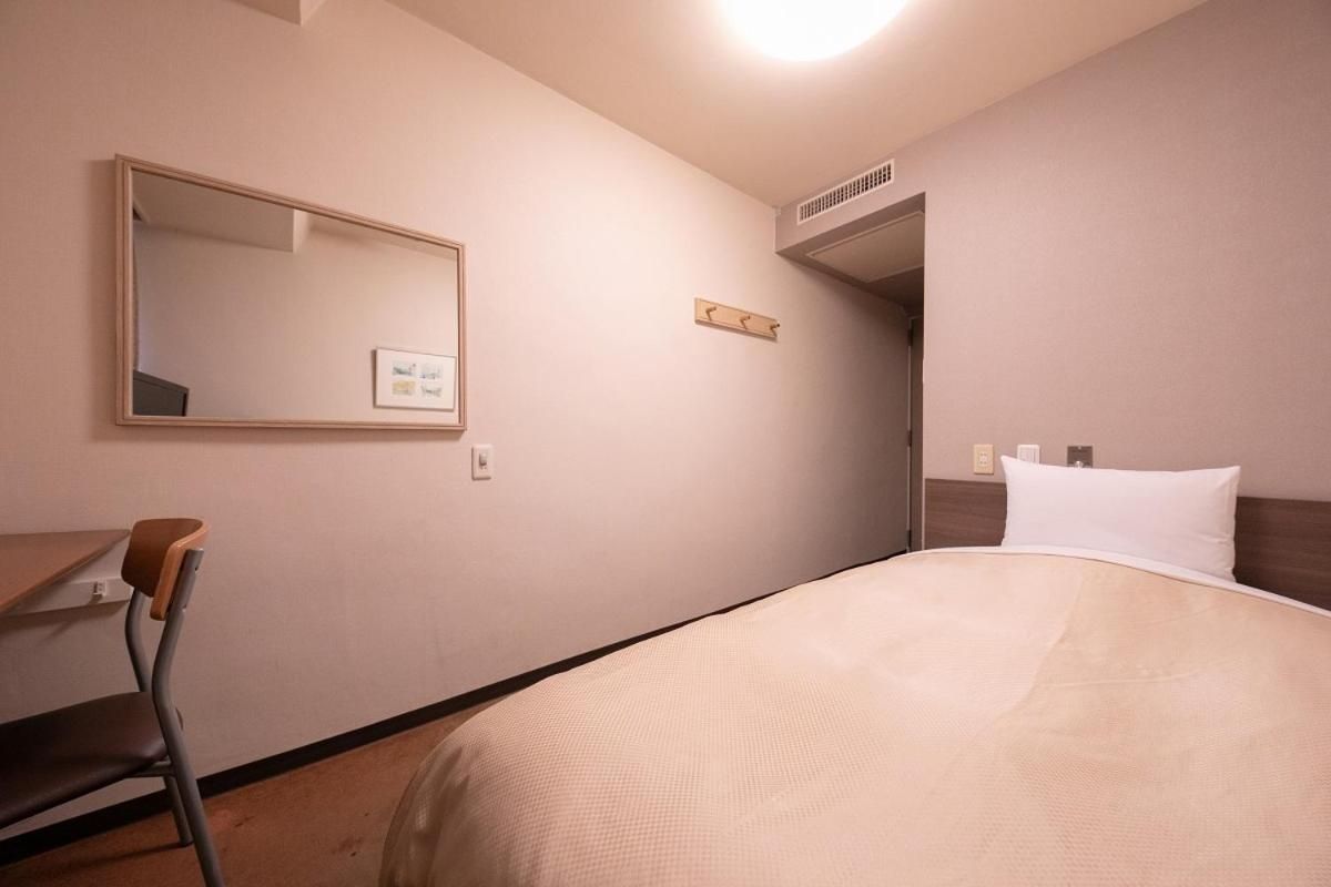 A hotel room with a bed, a desk, a chair, a mirror, and a door.