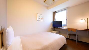 A hotel room with a bed, a desk with a computer, a chair, a television, and a window.