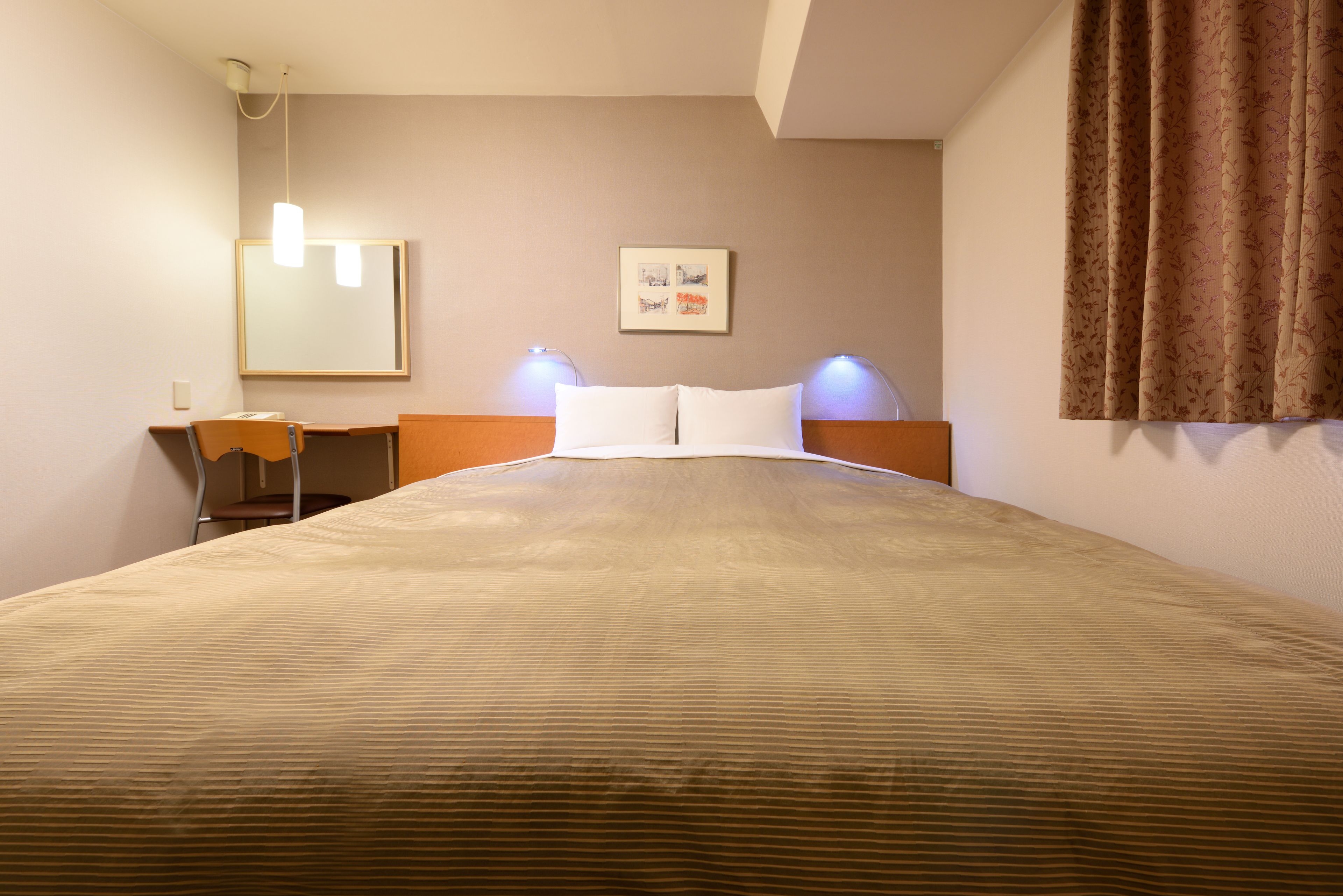 A hotel room with a large bed, a desk with a chair, a wall-mounted mirror, and two bedside lamps.