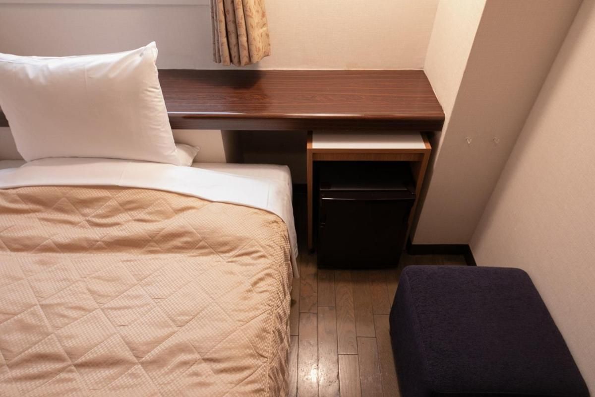 Una habitación de hotel compacta con una cama, un escritorio pequeño y un banco.
