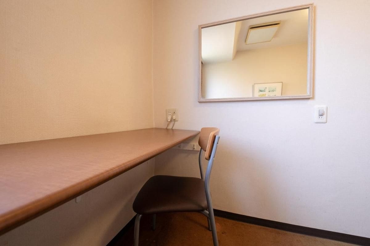 Ein Zimmer mit einem Holztisch, einem Stuhl, einem Wandspiegel und einem Lichtschalter.