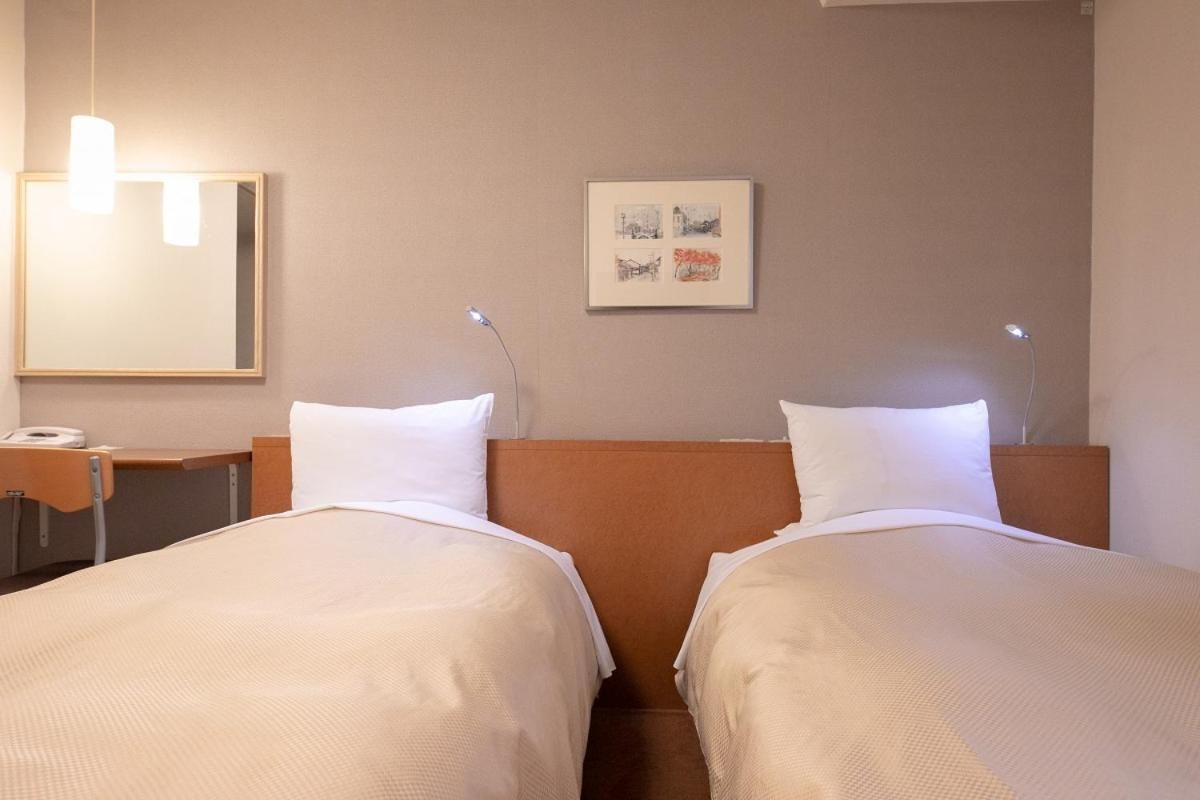 A hotel room with two beds, a bedside table, a lamp, and a framed picture on the wall.