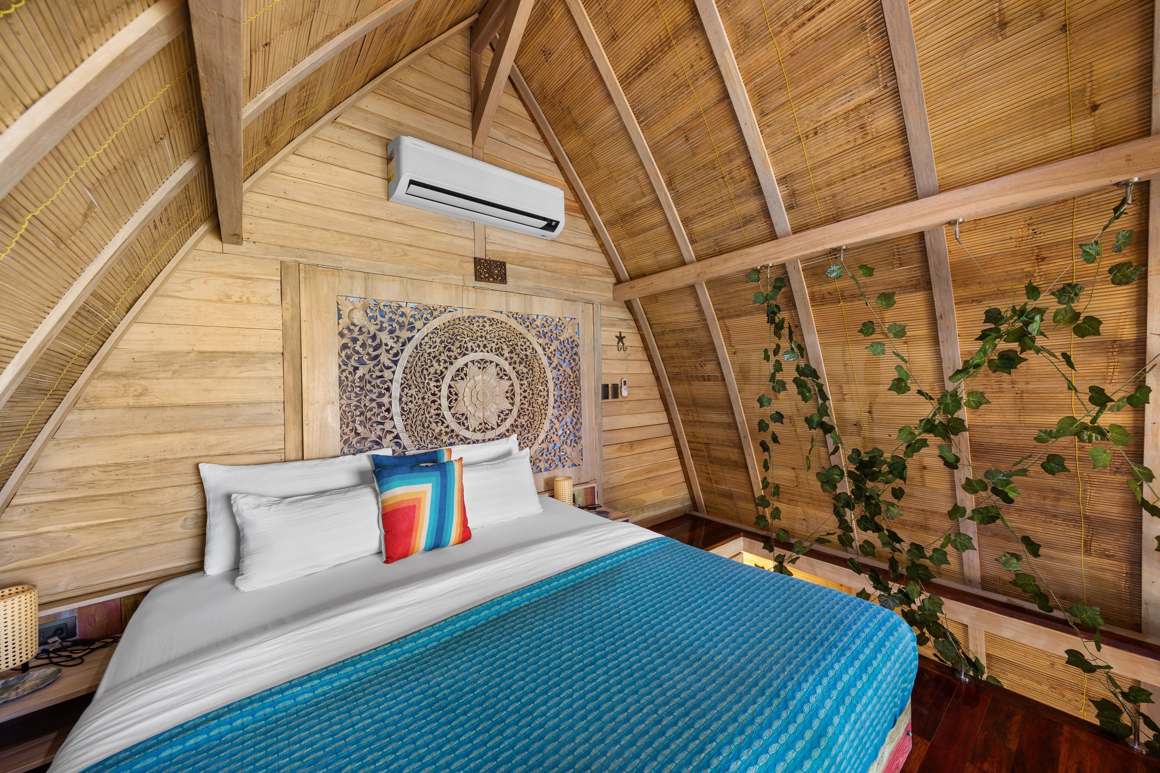 A bedroom with a sloped wooden ceiling, a bed with white and colorful bedding, and a decorative wall panel.