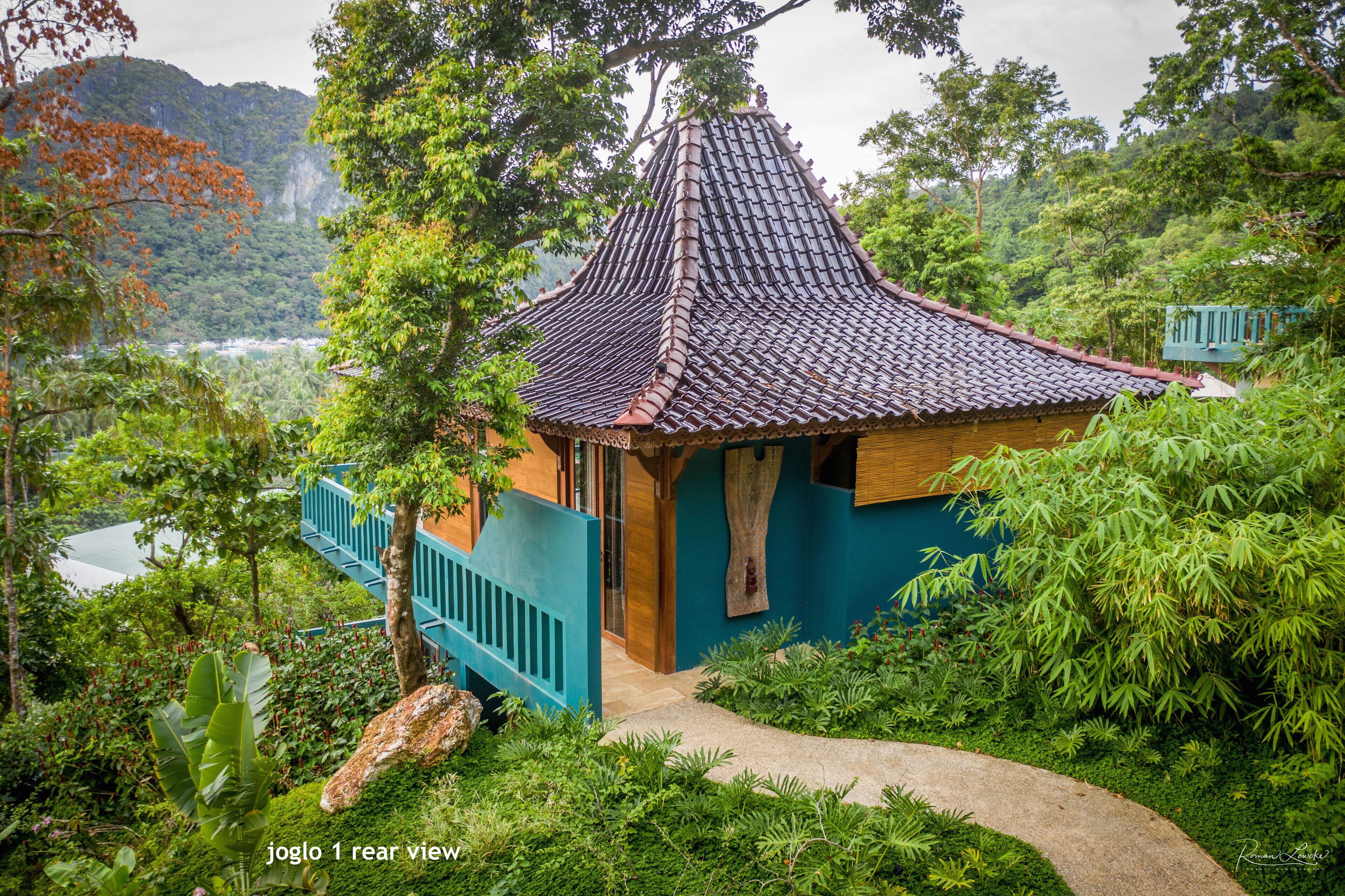 A traditional house with a tiled roof, surrounded by lush greenery and a view of a lake.