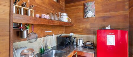 Cocina compacta con paredes de madera, un refrigerador rojo, pileta de acero inoxidable y diversos utensilios de cocina en estantes.