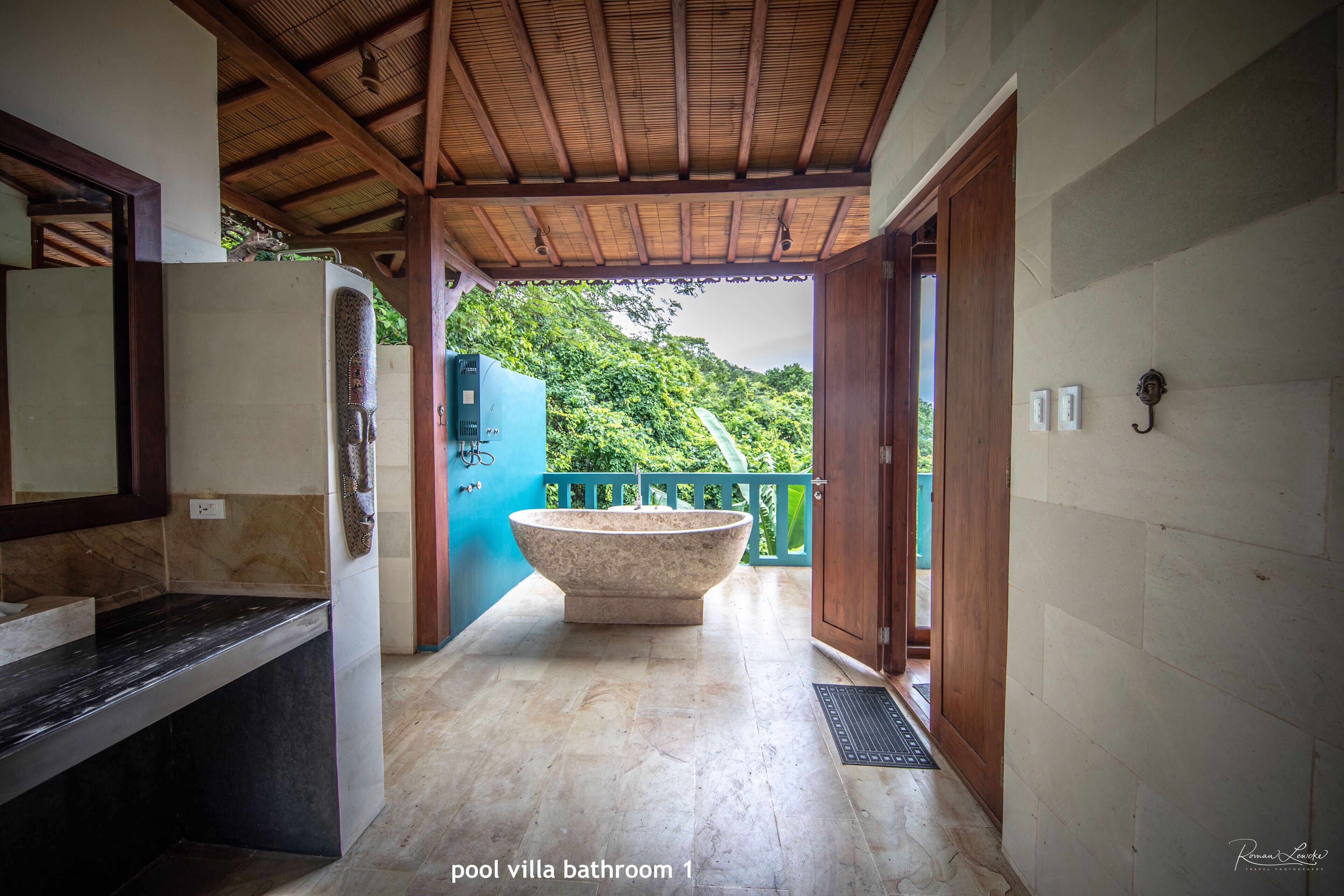 A bathroom with a freestanding bathtub, a marble countertop, and a view of lush greenery.