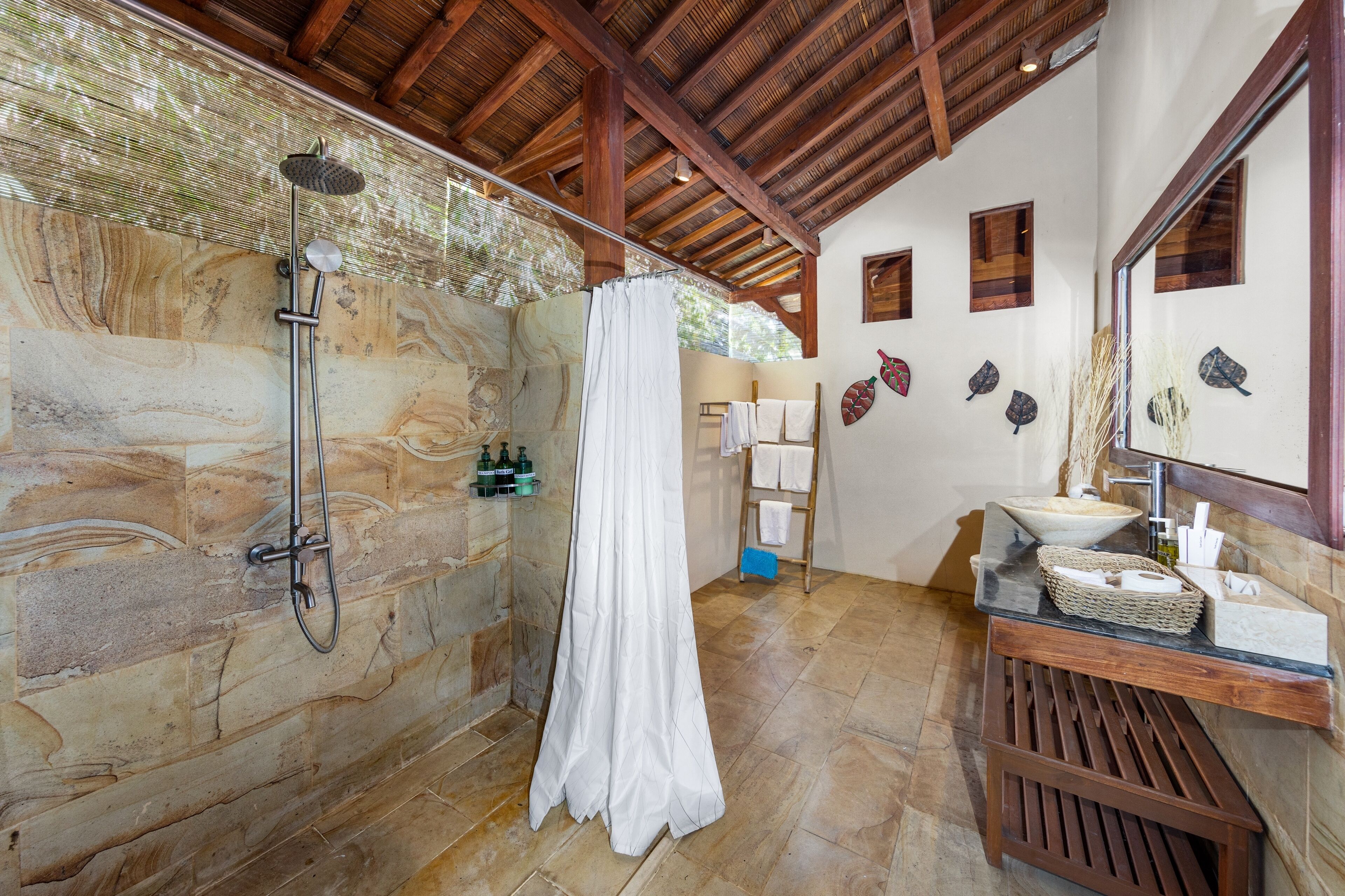 Une salle de bain aux murs en pierre, équipée d’une douche, d’un lavabo et d’un miroir.