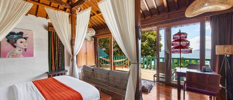 Una habitación con cama, un banco, una mesa y una silla. Hay un ventanal con vistas a una pagoda y vegetación.