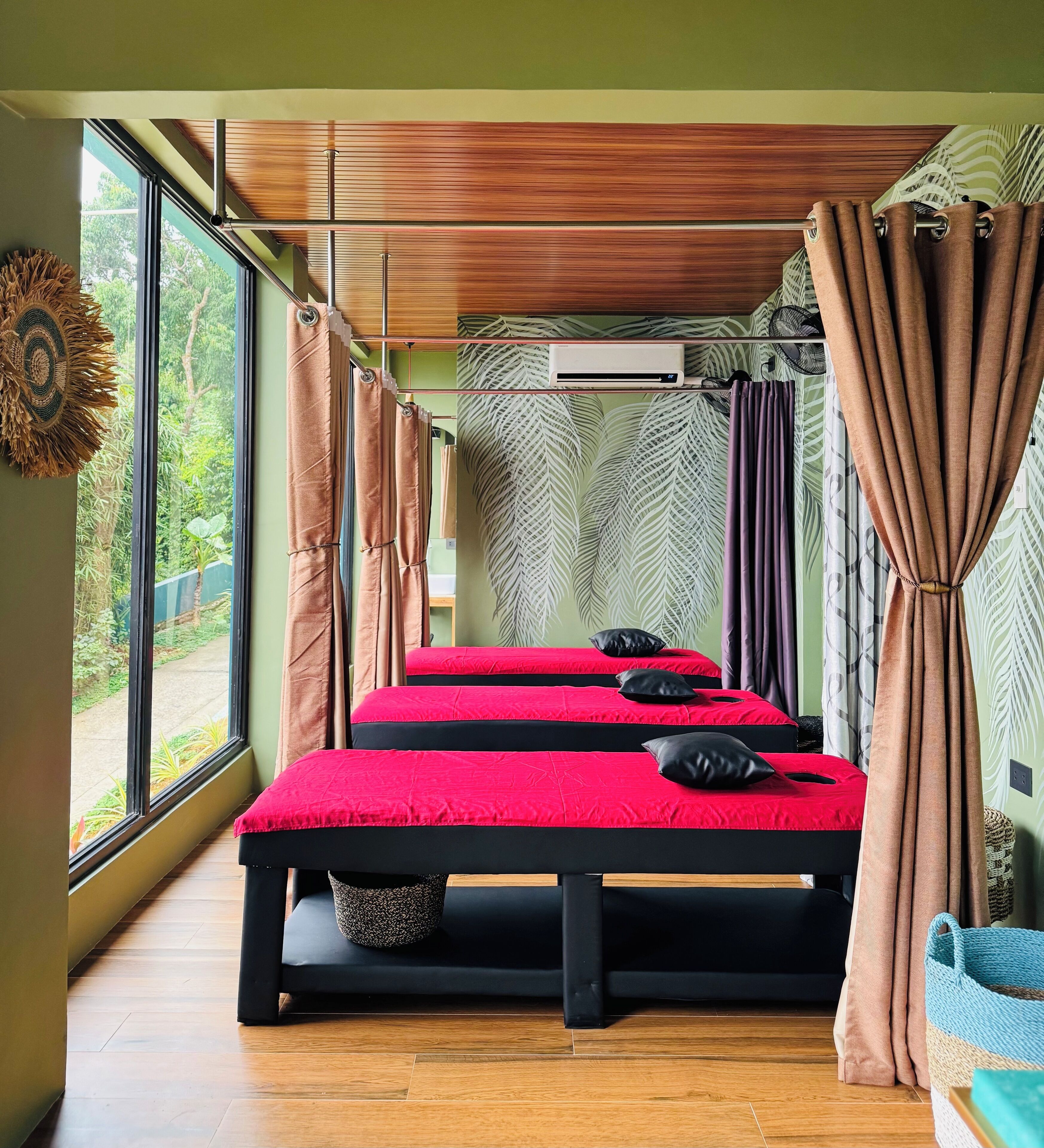 Ein Zimmer mit drei Betten, großen Fenstern und Blick auf Grünfläche.