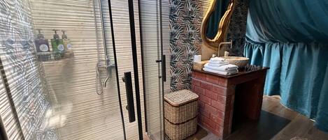 Un baño con cabina de ducha de vidrio, tocador de madera con lavamanos y un espejo.