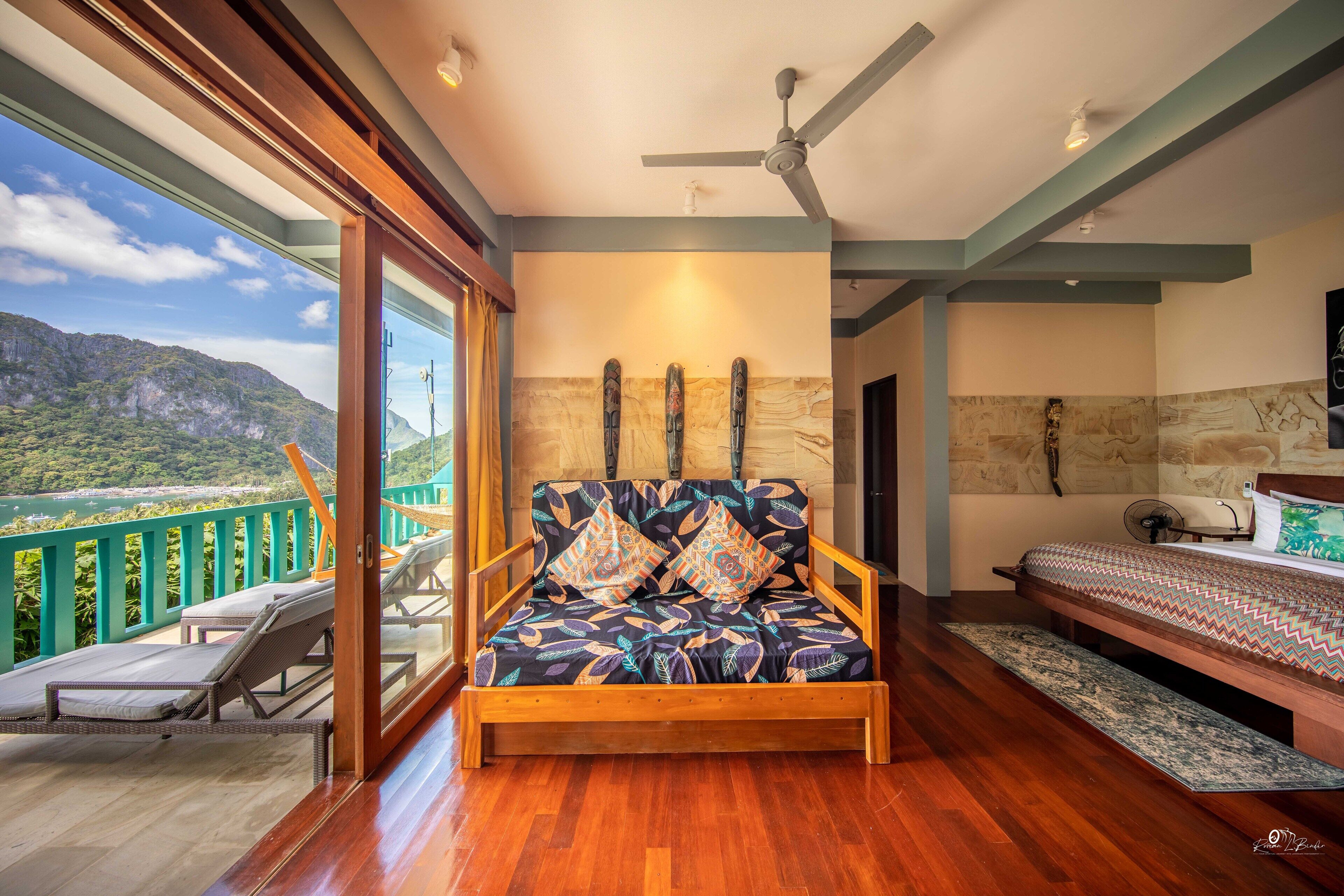 A room with a wooden sofa, a bed, and a balcony with a view of mountains.