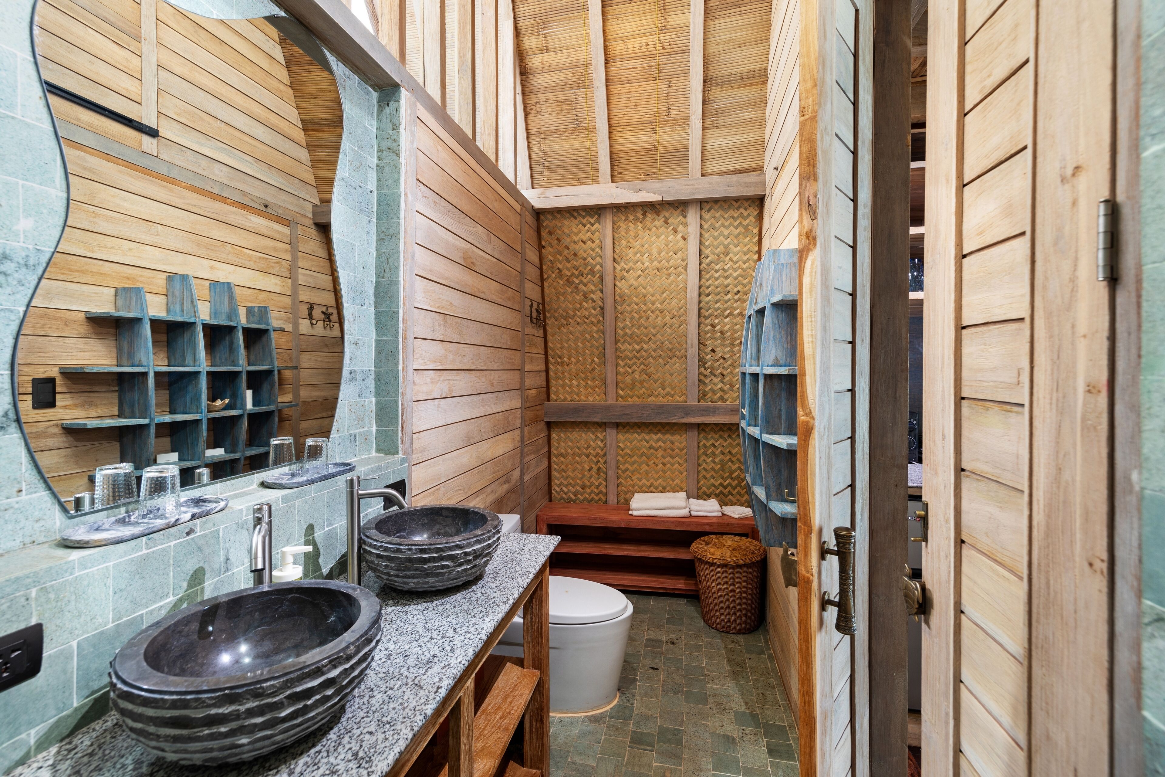 Une petite salle de bain aux murs en bois, dotée d’un grand miroir et de deux vasques en pierre.