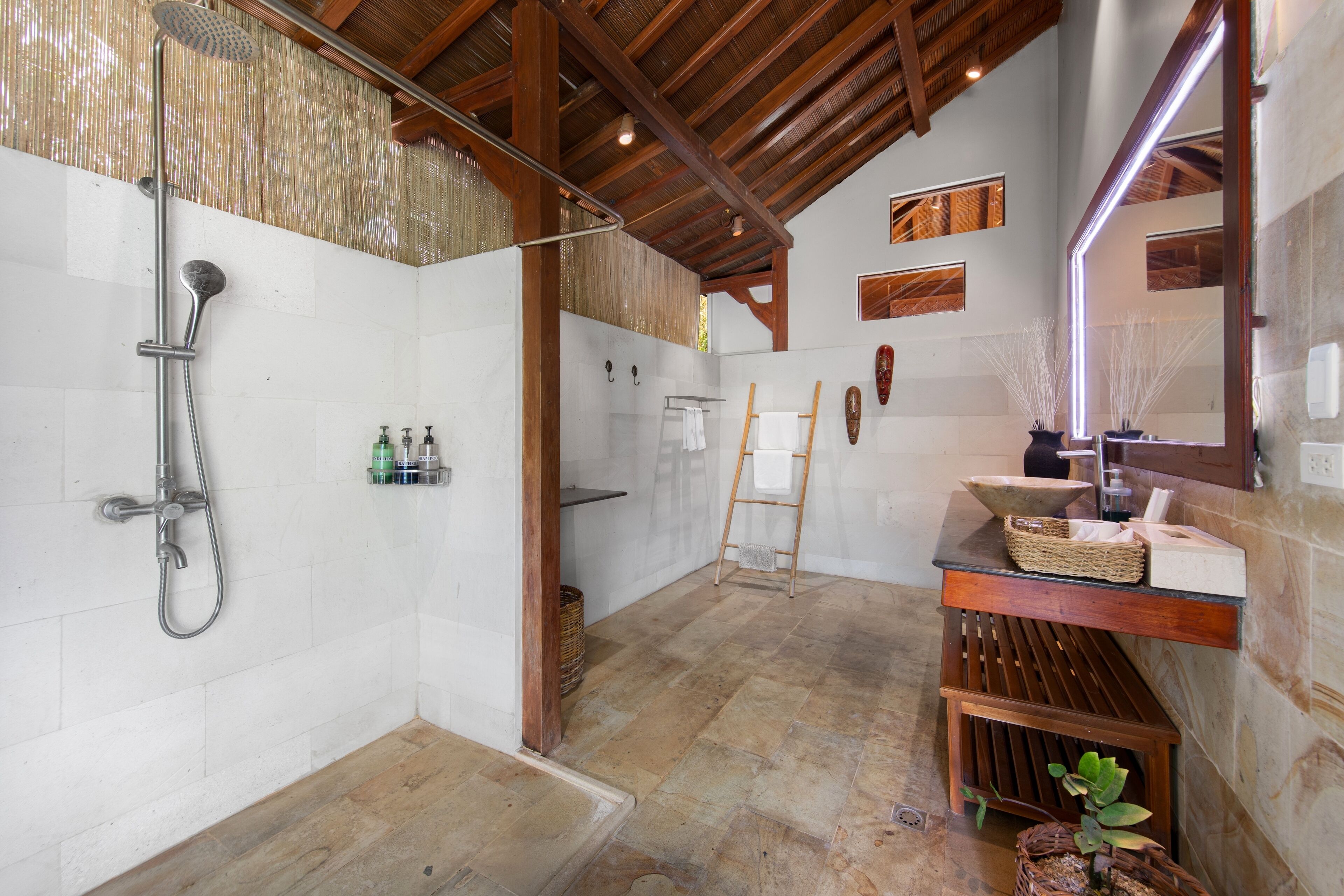 Une salle de bain spacieuse avec une douche, un banc en bois, un lavabo avec un miroir et un porte-serviettes.