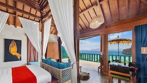 A room with a bed, a wicker chair, a desk, and a view of the sea.