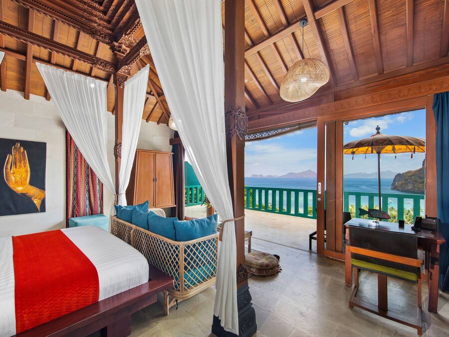 Una habitación con una cama, una silla de mimbre, un escritorio y vistas al mar.