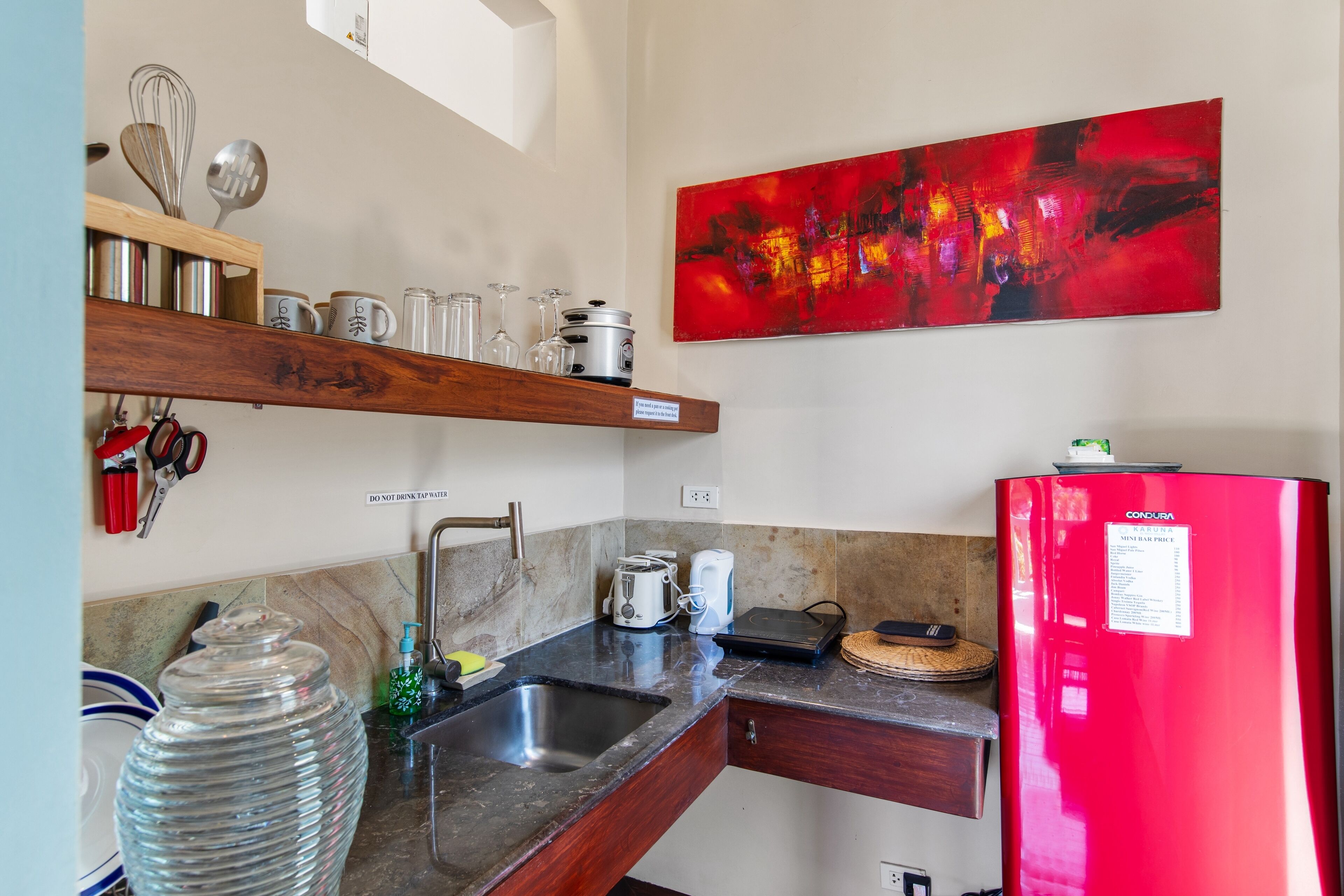 A kitchen with a red refrigerator, a sink, a coffee maker, and a shelf with kitchen utensils.