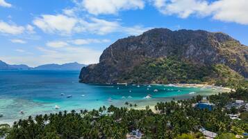 Un paisaje costero con una montaña imponente, aguas turquesas cristalinas y una zona de playa con palmeras.