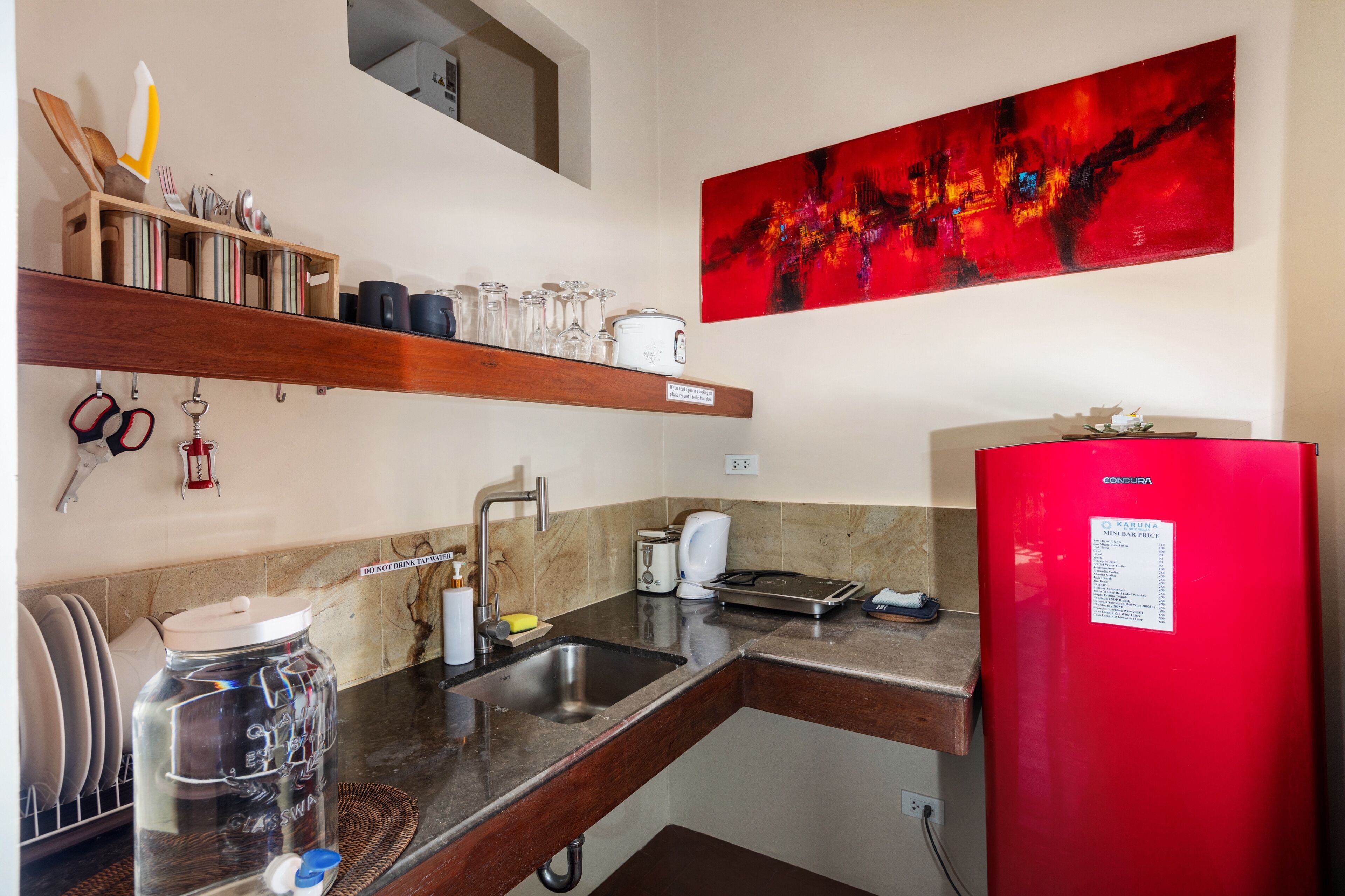 Cocina compacta con un refrigerador rojo, cafetera y lavamanos.