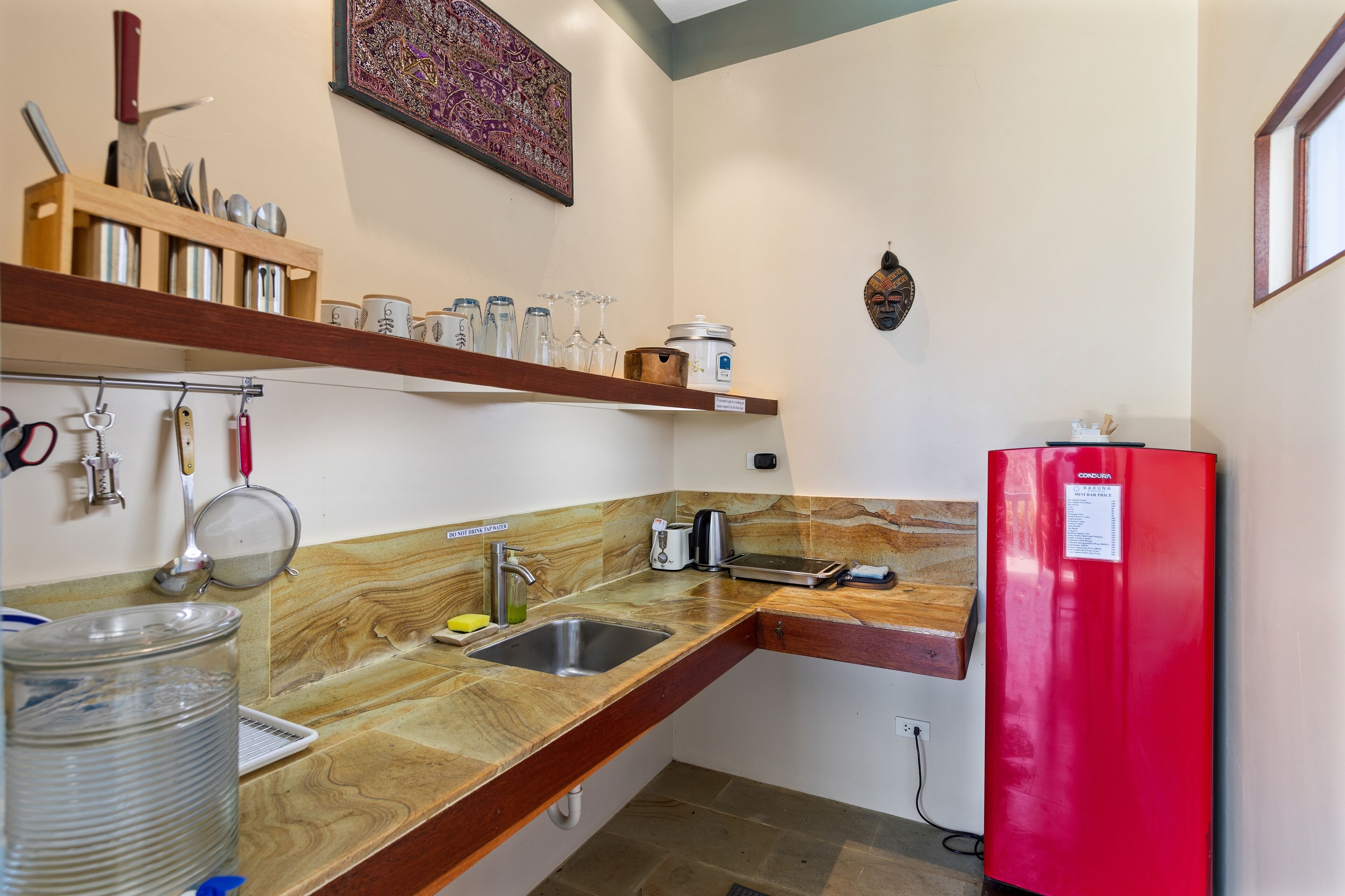 Una cocina compacta con un refrigerador rojo, estantes de madera y una encimera de piedra.