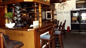A bar area with wooden bar stools, a counter with a bowl and glasses, and a refrigerator with a menu display. - Hotel-Restaurant Dümptener Hof (Muelheim an der Ruhr)