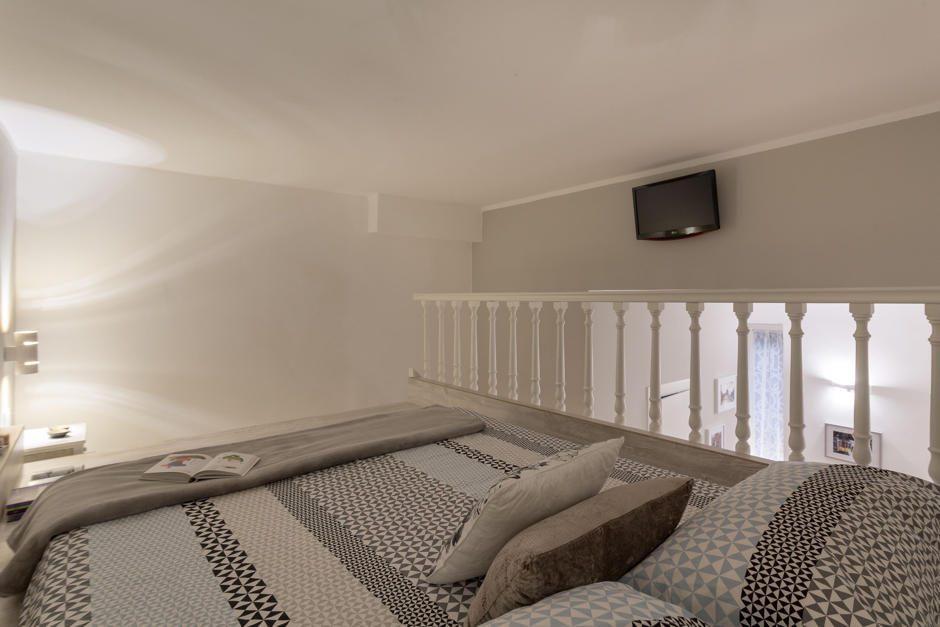 A bedroom with a bed, a TV mounted on the wall, and a balcony with a railing.
